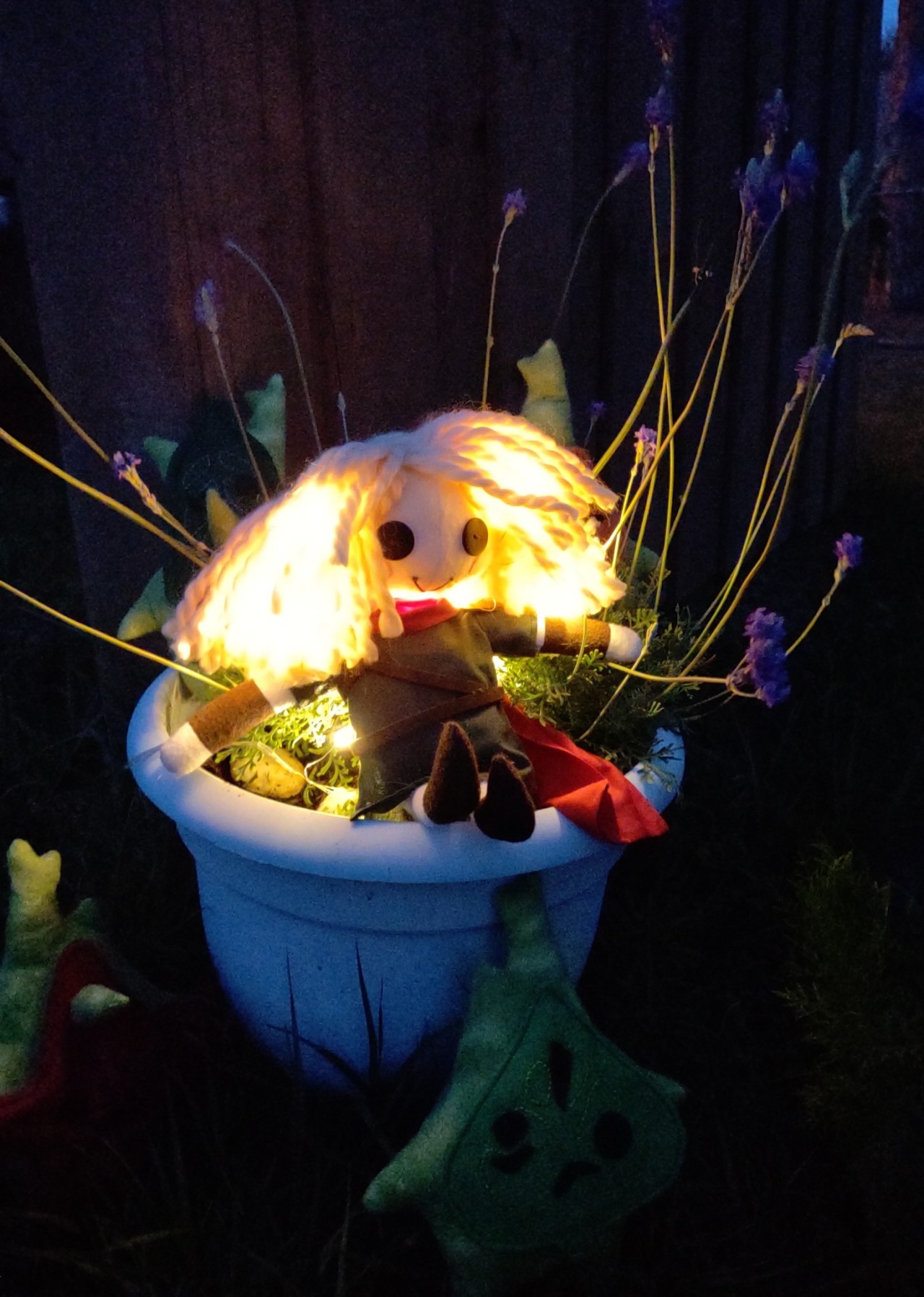 A button-eye doll of the first hero, sitting with a potted plant with lights so it looks as if he's glowing.
